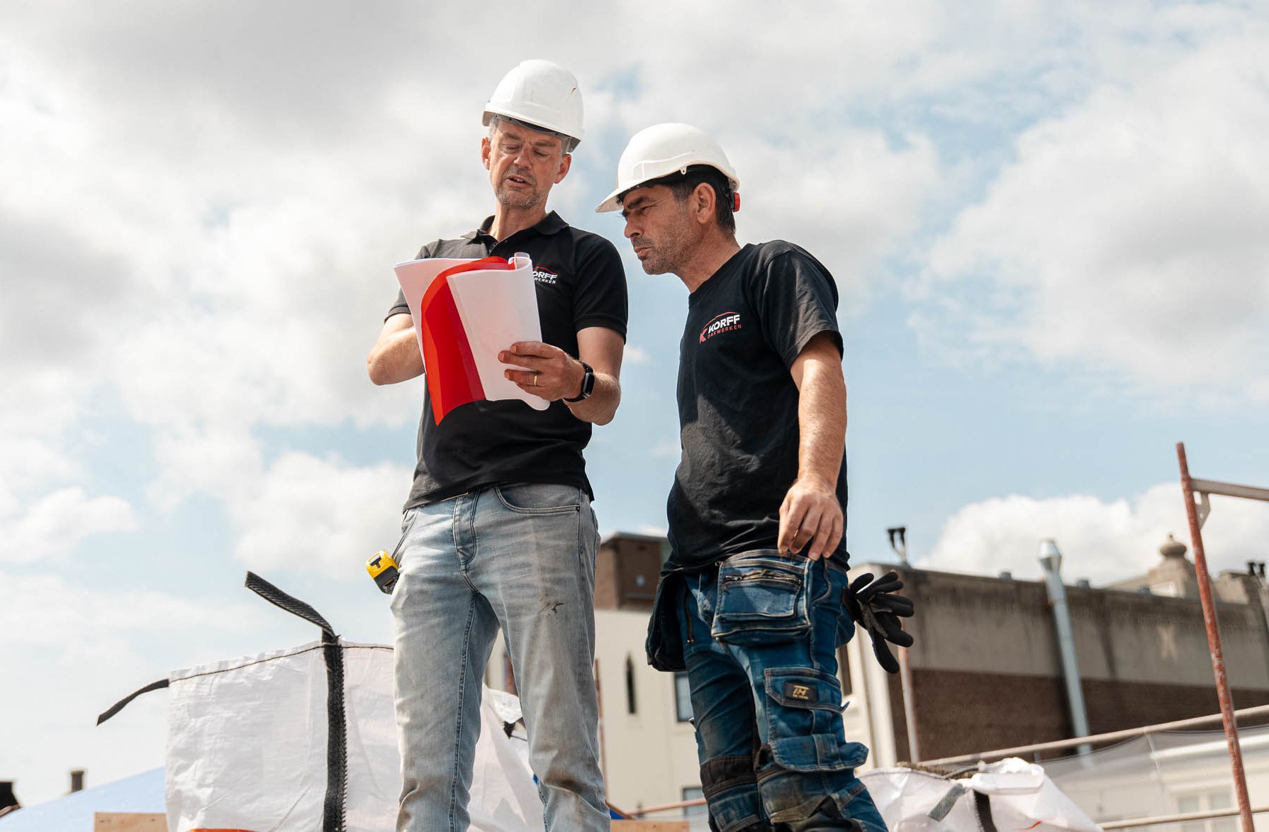Twee medewerkers van Korff Dakwerken bespreken bouwtekeningen en de uitvoering van dakwerkzaamheden op locatie.