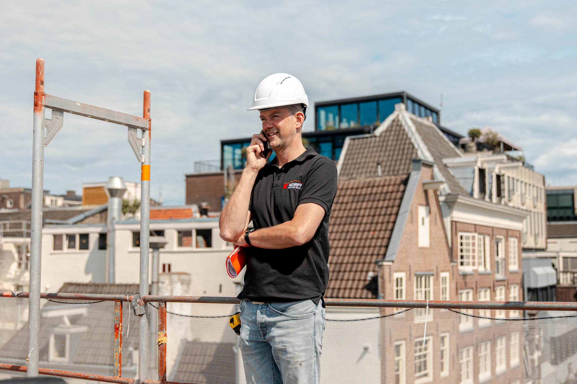 Uitvoerder van Korff Dakwerken belt tijdens werkzaamheden op een dak en houdt toezicht op het project.
