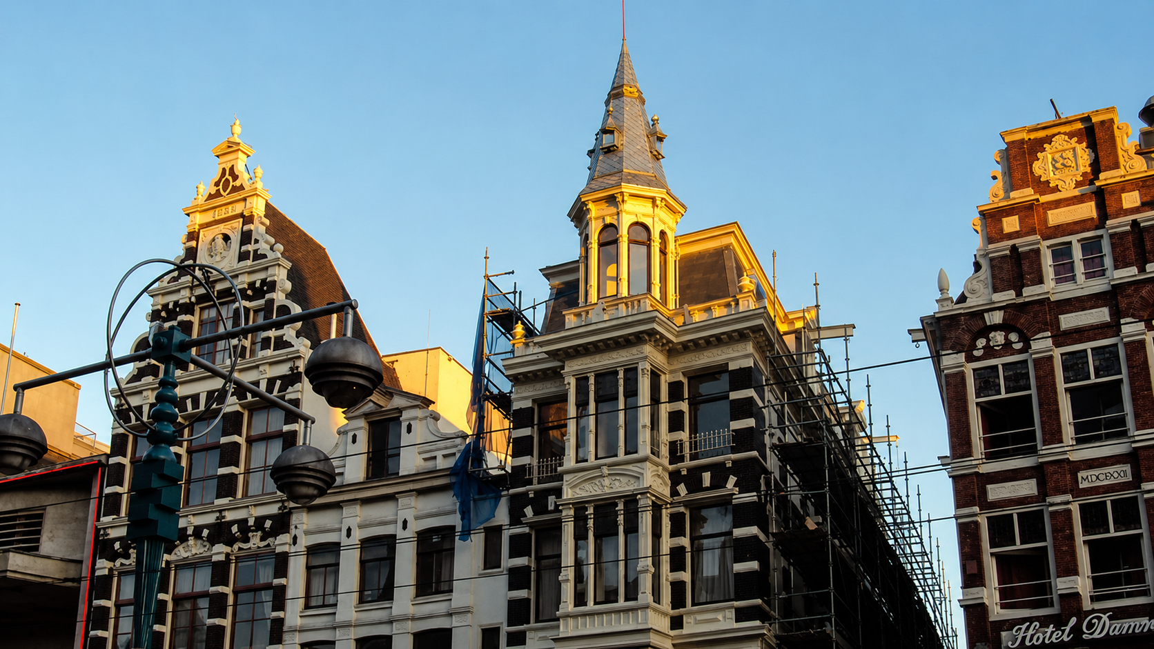 Monumentale gevels aan het Damrak in Amsterdam met steigers rond het pand tijdens de dakrenovatie.
